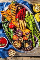 Hot vegetable salad. Set different grilled vegetables on a plate. Vegan barbeque picnic set, with asparagus, tomatoes, mushrooms, peppers, corn and sauces