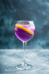 Colorful cocktail with lemon and lavender liqueur in wineglass on the rustic background. Selective focus. Shallow depth of field.
