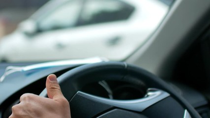 POV with selective focusing to hand holding car's steering wheel while driving a car.
