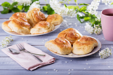sweet buns on ceramic plate, blossom branches on white wooden background
