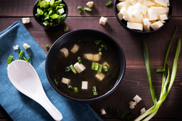 Japanese hot miso soup in a black bowl on the wooden table. Horizontal view from above