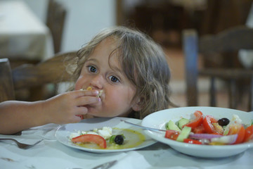 a 4 year old girl eats Greek food in a tavern
