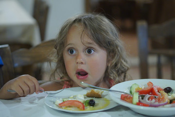 a 4 year old girl eats Greek food in a tavern