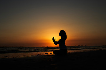 Fototapeta na wymiar silhouette of woman practicing yoga on the beach at sunset