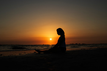 Fototapeta na wymiar silhouette of woman practicing yoga on the beach at sunset
