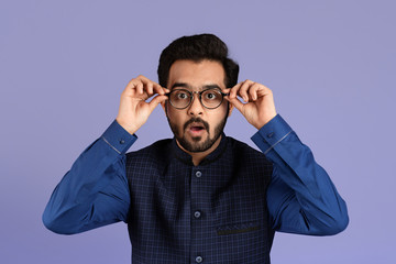 Millennial Indian guy opening mouth in surprise on lilac background