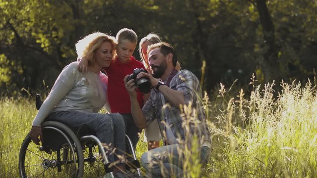The father photographs the family with a professional camera. Family with a disabled mom in a wheelchair take a family photo with children in nature. Family concept. Toned footage. Prores 422. 