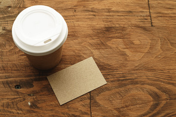 Takeaway coffee cup with blank business card on wooden table
