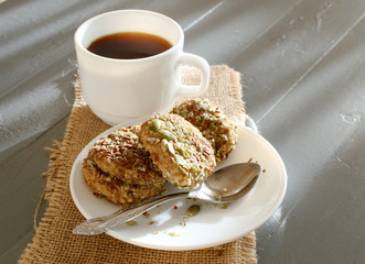 white cup with coffee next to baking on a plate. baking made of banana sesame seeds and pumpkin seeds.