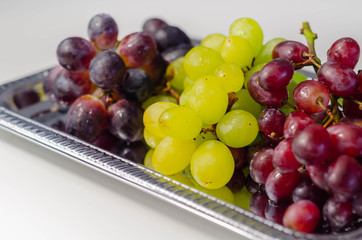 Three types of green, red and black grapes on a silver tray