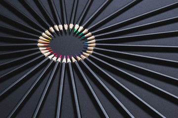 Colored pencil set arranged in circle on black background. Stationery backdrop for your design.