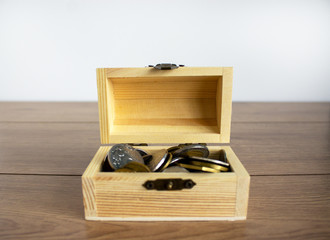 Concept business image. Small chest with coins on a beautiful wooden table. White background, copy space.