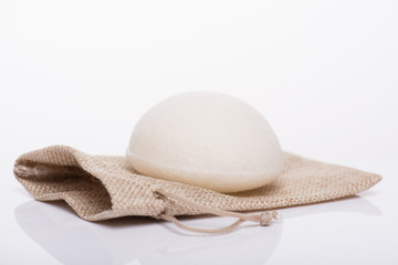 Close-up photo of white konjac sponge without additives lying on craft small case package bag isolated on white background