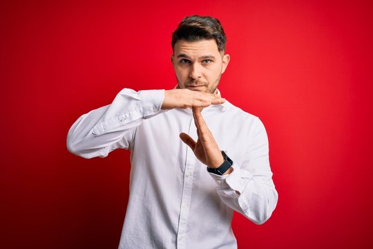 Young business man with blue eyes wearing elegant shirt standing over red isolated background Doing time out gesture with hands, frustrated and serious face