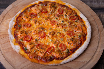 Pizza with salmon, tomatoes and capers on a wooden board. Whole pizza. Close-up.