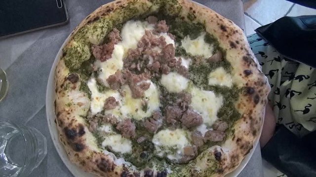 A pizza with mozzarella, cream, pieces of sausage and broccoli rabe.
