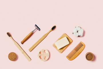 Bathroom accessories on pink background. Natural bamboo toothbrush, sponges, cotton flowers, shaving brush. Flat lay, top view.