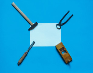 Carpentry tools on an aquamarine background with a white lettering sheet in the center