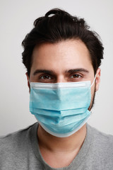 Vertical close-up of young caucasian man in a blue medical mask on his face. Theme of coronavirus and safety. 
