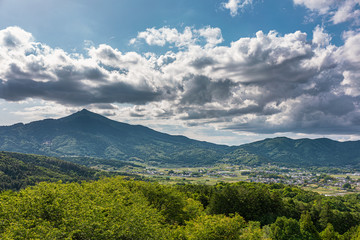 太陽光に照らされた大きな雲と新緑の里山