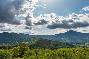 太陽光に照らされた大きな雲と新緑の里山