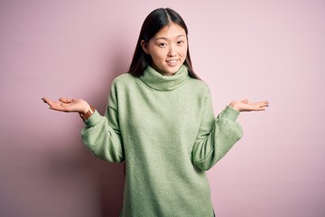 Young beautiful asian woman wearing green winter sweater over pink solated background smiling showing both hands open palms, presenting and advertising comparison and balance