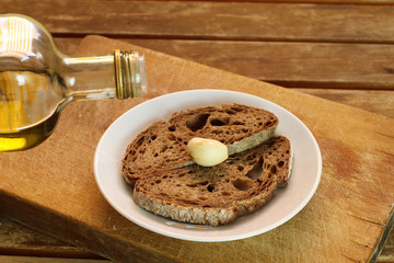 White ceramic plate with slices of bread, clove of garlic and bottle of oil. Wooden cutting board