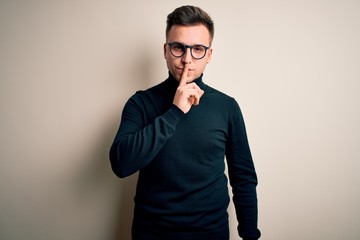 Fototapeta premium Young handsome caucasian man wearing glasses and casual sweater over isolated background asking to be quiet with finger on lips. Silence and secret concept.