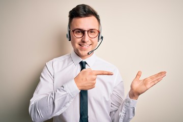 Young handsome caucasian business man wearing call center headset at customer service amazed and smiling to the camera while presenting with hand and pointing with finger.