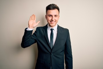 Young handsome business man wearing elegant suit and tie over isolated background Waiving saying hello happy and smiling, friendly welcome gesture