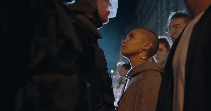 Young female protestor stepping forward and staring at the policeman with anger. Group of social activists protesting silently in front of police force.
