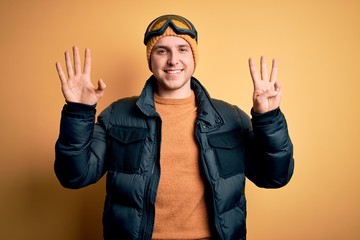 Young handsome caucasian man wearing hat, coat and ski glasses for winter and snow weather showing and pointing up with fingers number eight while smiling confident and happy.