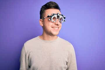 Obraz premium Young handsome caucasian man wearing optometrical glasses over purple background looking away to side with smile on face, natural expression. Laughing confident.