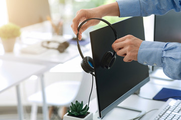 Contact center worker placing his headset on computer monitor at office, closeup of hands. Copy...