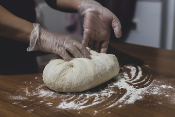 Hands of a woman making dough with plastic gloves on the table