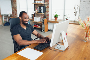 Smiling. Young man, businessman working in office, looking on blank black computer screen, monitor. Copyspace for your ad. Finance, business, work, gadgets and tech concept. Freelance, remote worker.