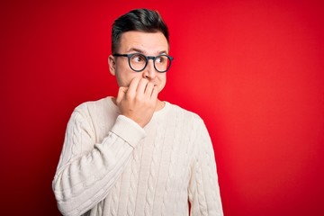 Young handsome caucasian man wearing glasses and casual winter sweater over red background looking stressed and nervous with hands on mouth biting nails. Anxiety problem.