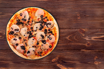 Delicious pizza with ham, mozzarella, mushrooms and olives on a round slate platter which is on the wooden table, top view and copy space