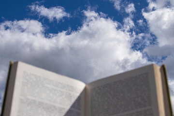  Blurry pages of an open book, on a background of blue sky with clouds.