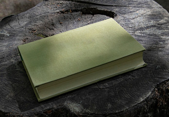 Closed book, hardcover, on a wooden slice of an old tree.