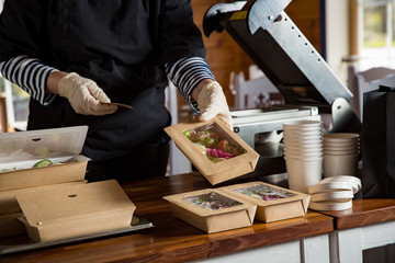 Restaurant worker wearing protective mask and gloves packing food boxed take away. Food delivery services and Online contactless food shopping.