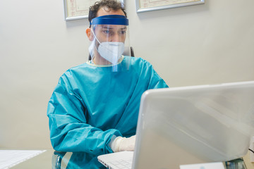 A professional in his office working on the computer with the necessary protection measures to avoid the Covid 19 virus: mask and gloves.