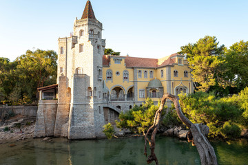 The Palácio dos Condes de Castro Guimarães illuminated by the sun with tourists bathing in the water at the bottom of the steps.