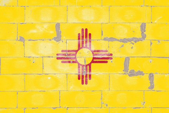 National flag of US state of New Mexico, the red sun sign, Zia symbol, yellow on Independence Day, against a background of a brick wall with peeling paint. Political and religious disputes, delivery.