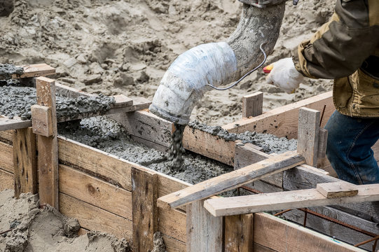 Pouring cement into a wooden formwork for the Foundation of a building that is being built.