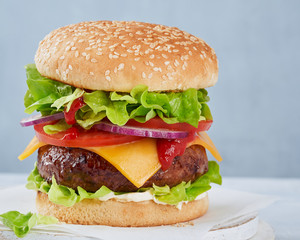 Close-up of a tasty hamburger sandwich containing: cooked patties of ground meat, onion, tomatoes, cheese, sauce fresh green salad on a light background, copy space. Fast food and barbecue collection.