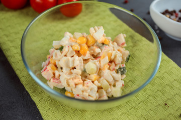 Russian traditional salad with corn, egg and crab meat, covered with mayonnaise on the green towel. 