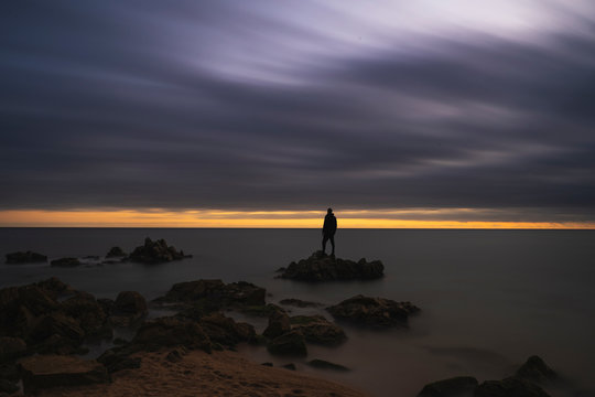 silueta de un hombre parado entre las rocas del mar mediterr&aacute;neo durante el atardecer