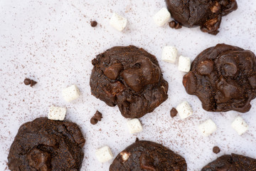 Top view of baked dark chocolate cookies with marshmallow, with their ingredients on white background.