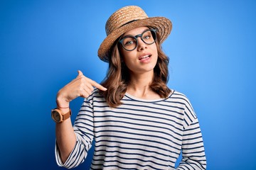 Young beautiful blonde girl wearing glasses and hat over blue isolated background with surprise face pointing finger to himself